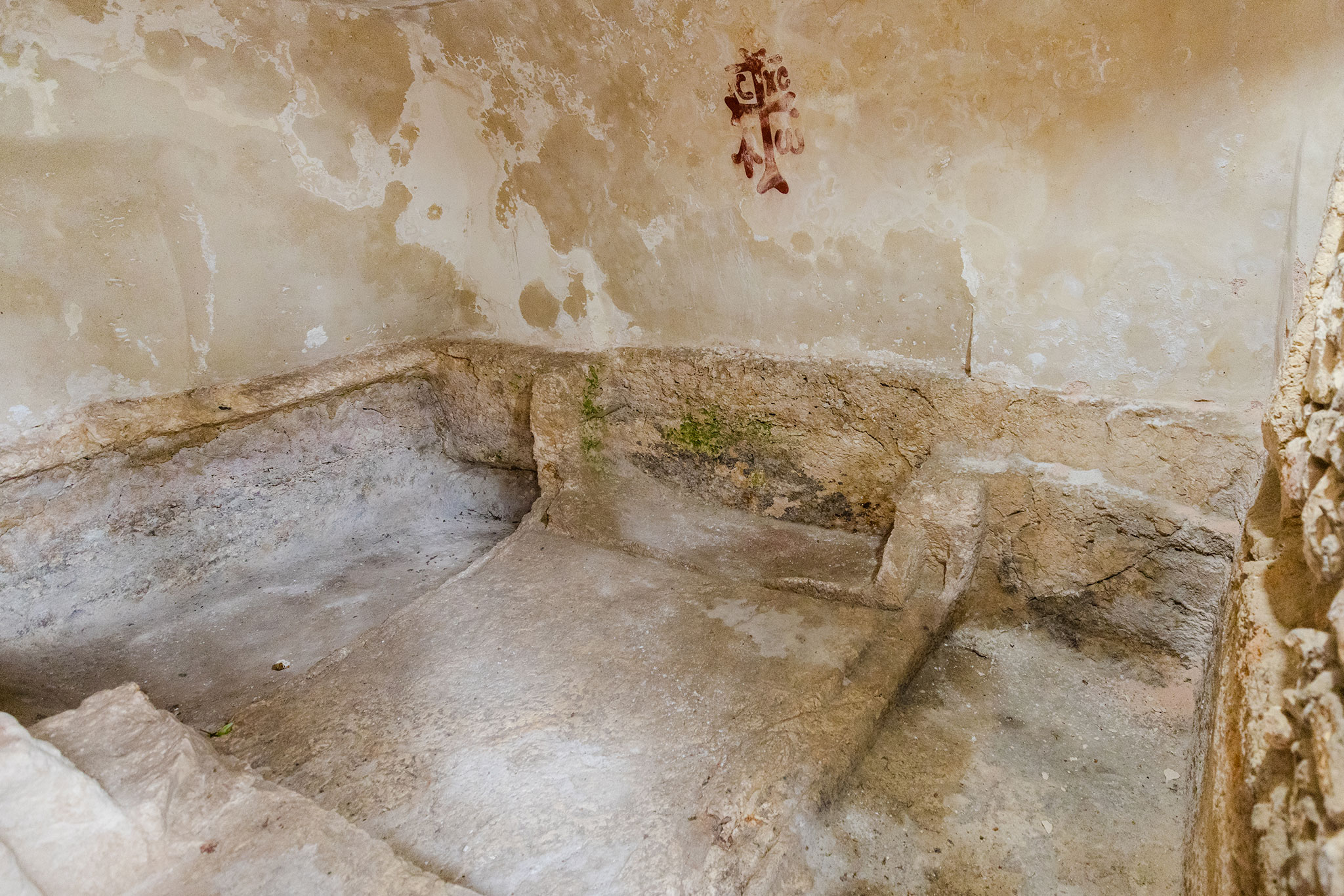 Ancient tomb room with worn stone benches and faded wall markings.
