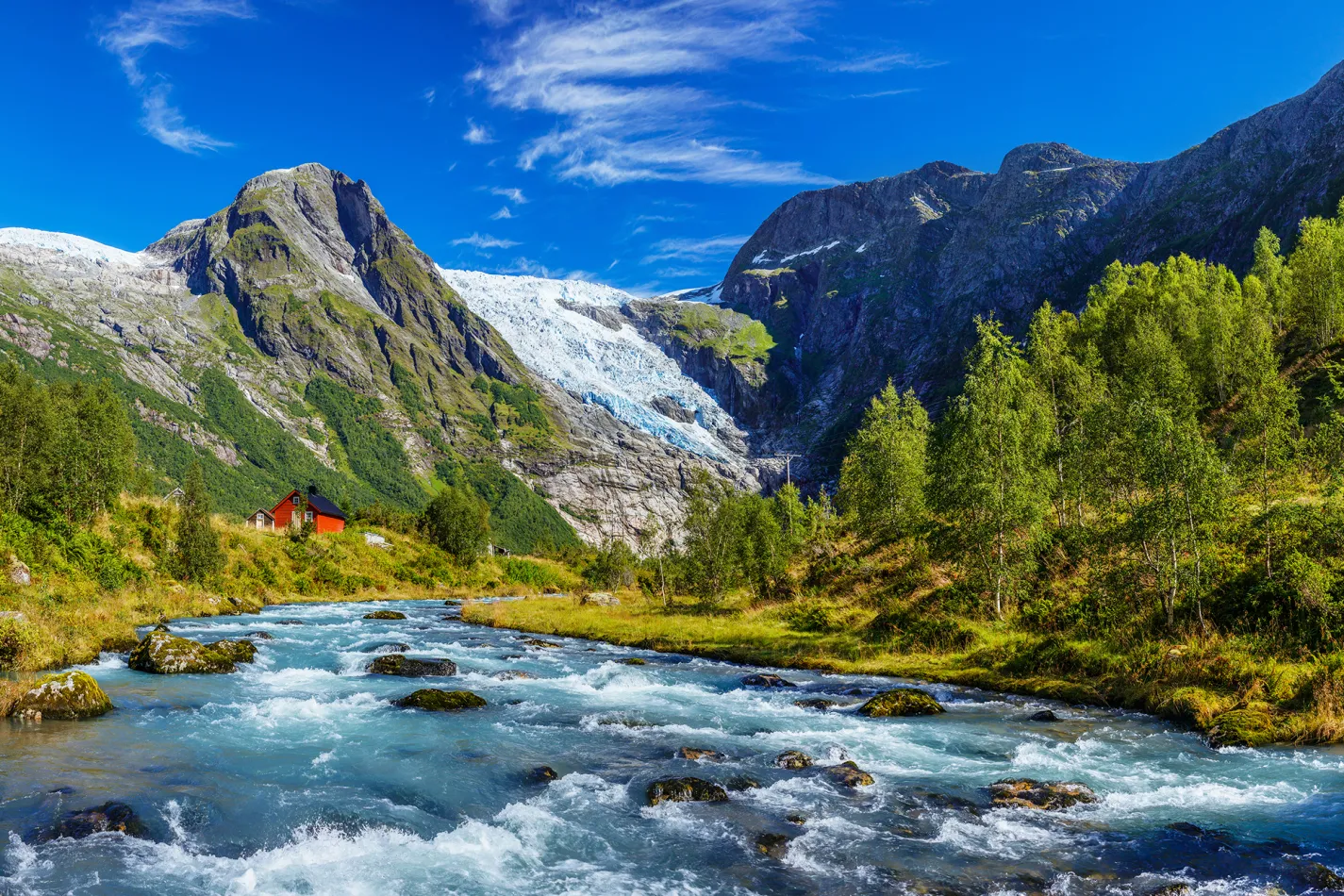 A rushing river surrounded by green trees and tall, snowy mountains