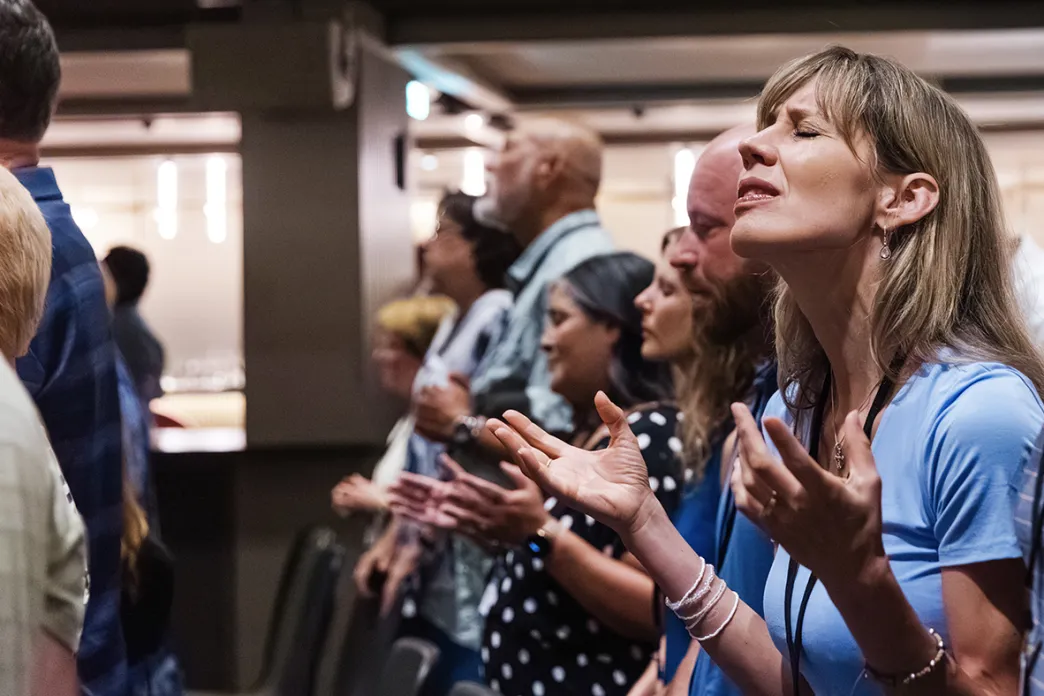 Woman standing in a crowd of people with eyes closed and hands lifted