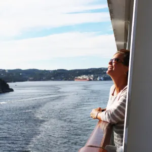 A smiling woman leaning on the ship deck railing, looking out over the water