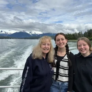 Three smiling women with the ocean and mountains in the background